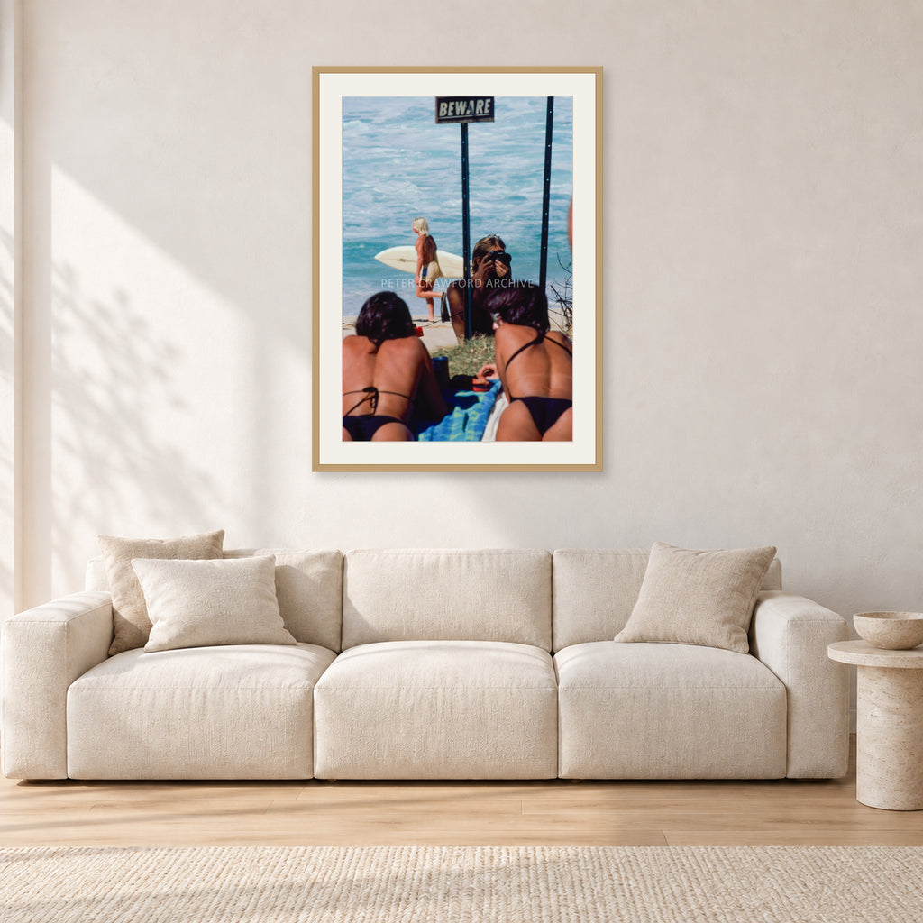 Beware Girls, 1985 by Peter Crawford — 60 × 90 cm, hayseed frame with white mat, shown in a light minimalist living room.