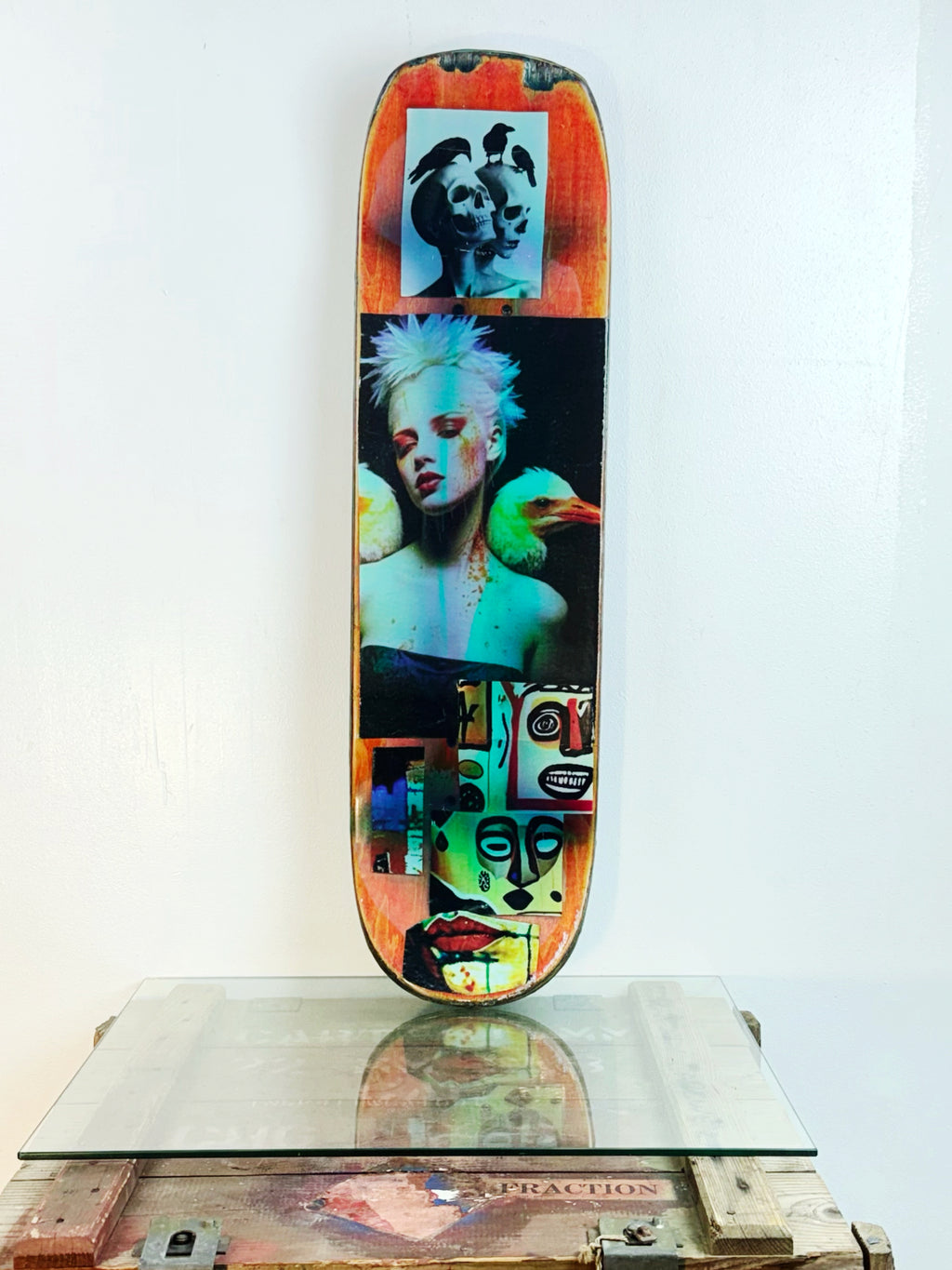 Skateboard 1 by David Bromley — colourful portraits and layered collage imagery on a skateboard deck, painted deck displayed above a glass-topped wooden crate.