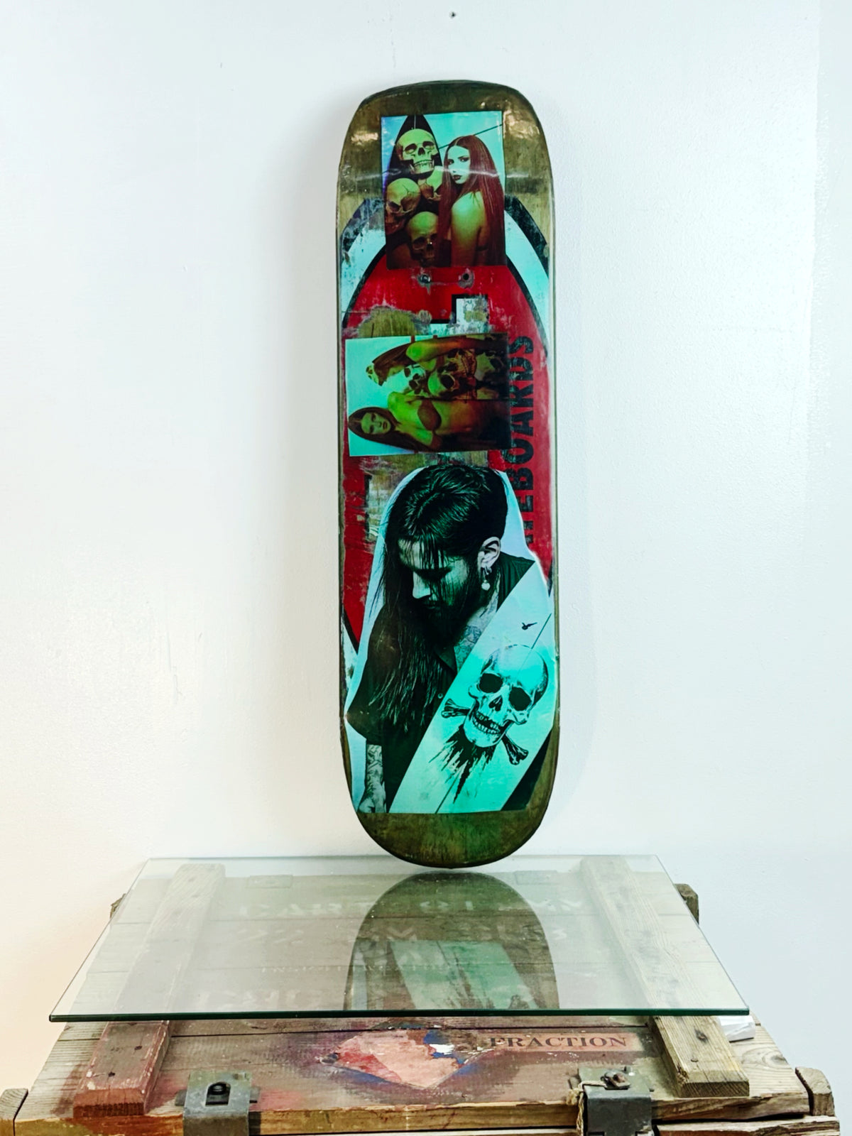 Skateboard 1 by David Bromley — colourful portraits and layered collage imagery on a skateboard deck, painted deck displayed above a glass-topped wooden crate.
