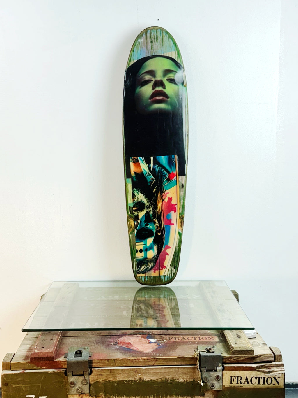 Skateboard 2 by David Bromley — portrait and seated-boy imagery on a green-toned skateboard deck, painted deck displayed above a glass-topped wooden crate.