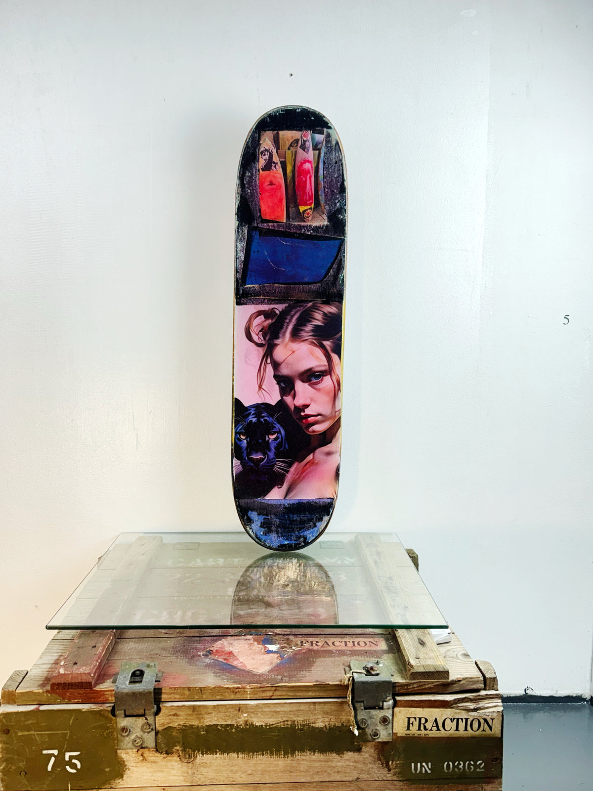 Skateboard 5 by David Bromley — pink and purple portrait collage on a skateboard deck, painted deck displayed above a glass-topped wooden crate.