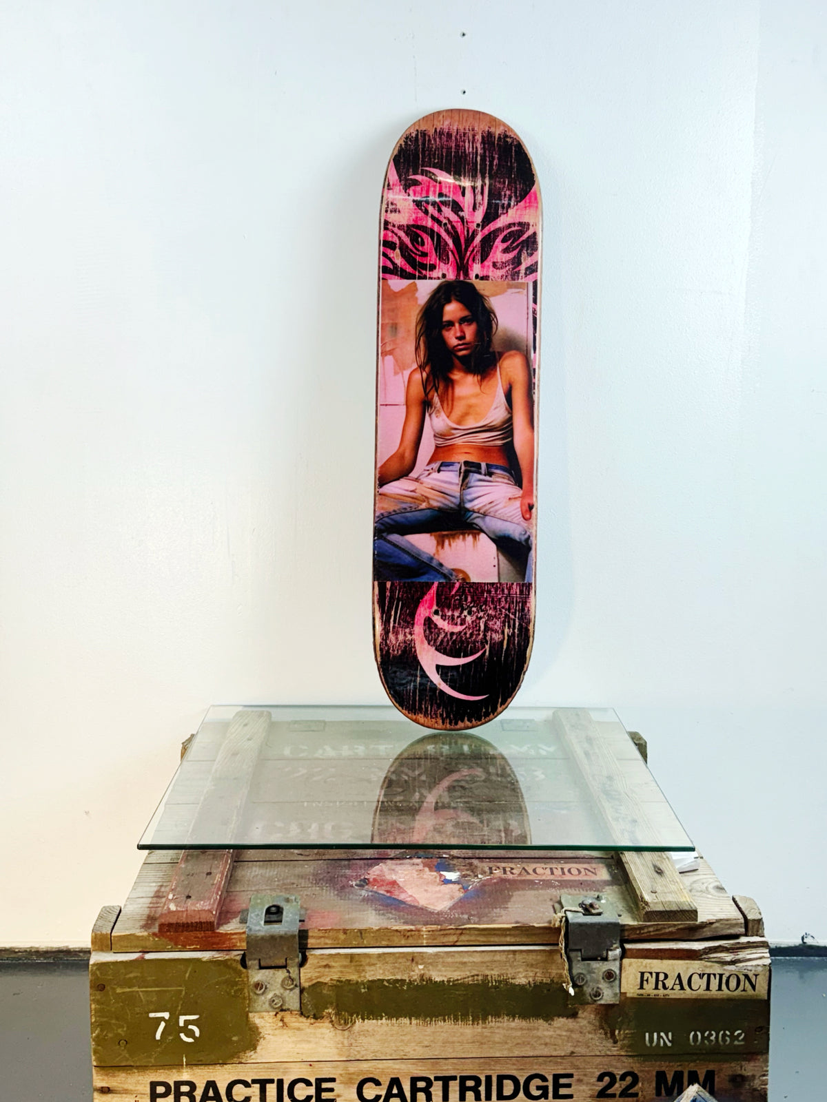 Skateboard 5 by David Bromley — pink and purple portrait collage on a skateboard deck, painted deck displayed above a glass-topped wooden crate.