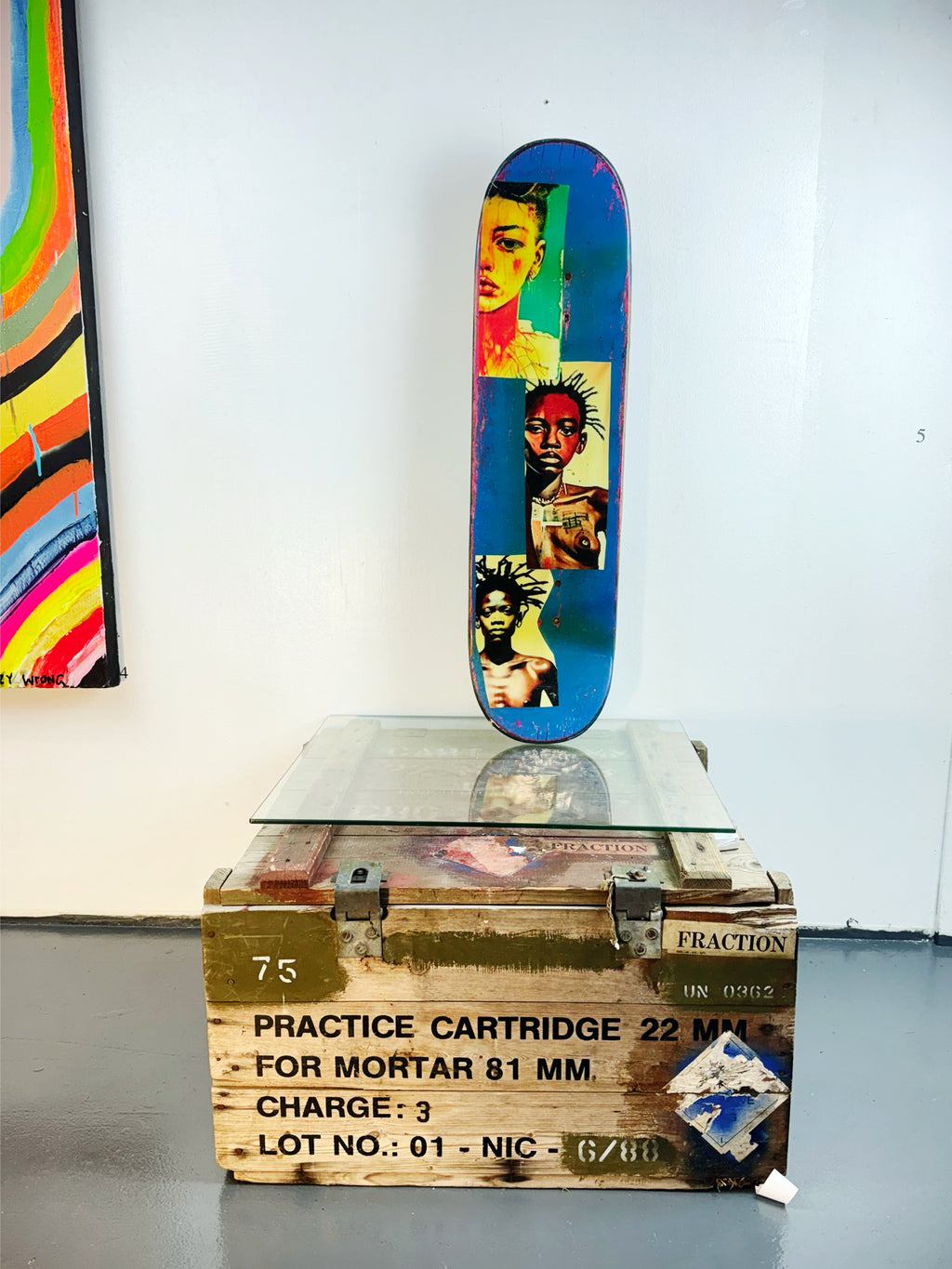 Skateboard 6 by David Bromley — portrait collage across blue and cream skateboard surfaces, painted deck displayed above a glass-topped wooden crate.