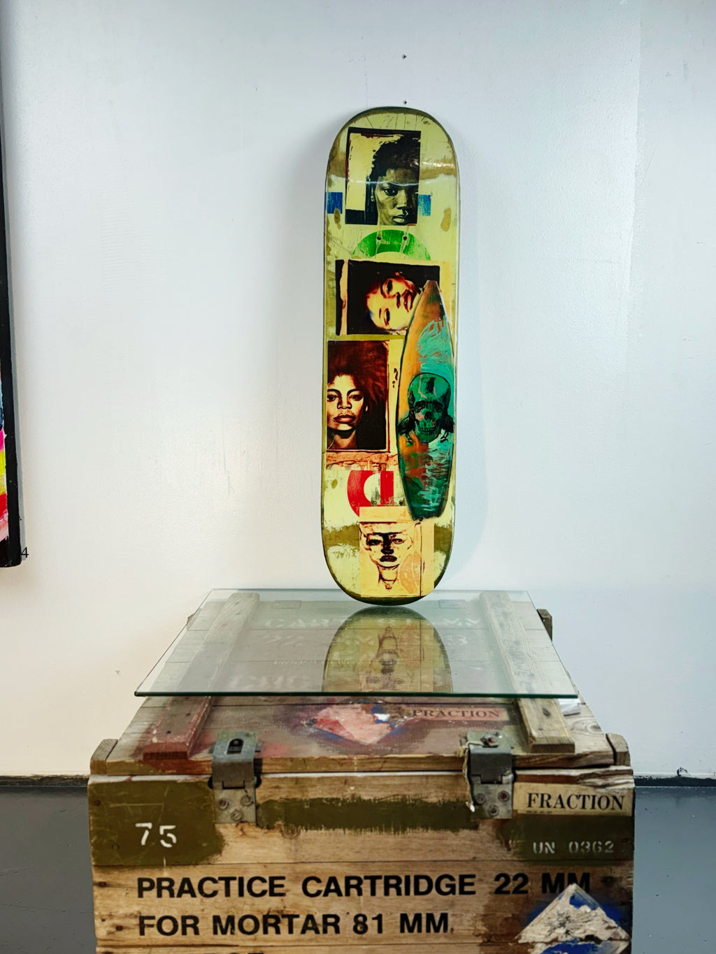 Skateboard 6 by David Bromley — portrait collage across blue and cream skateboard surfaces, painted deck displayed above a glass-topped wooden crate.