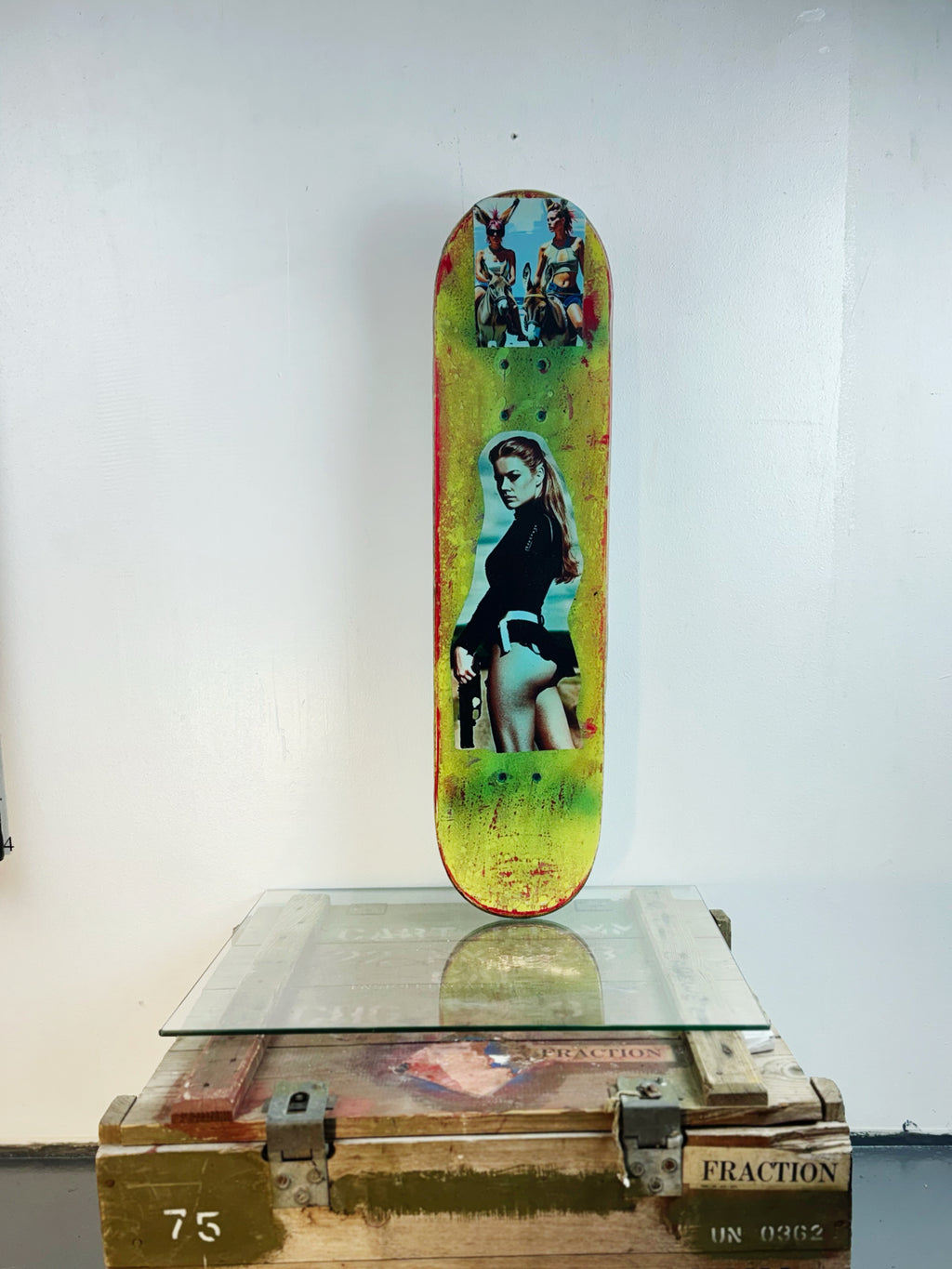 Skateboard 7 by David Bromley — portrait collage across green and pale blue skateboard surfaces, painted deck displayed above a glass-topped wooden crate.