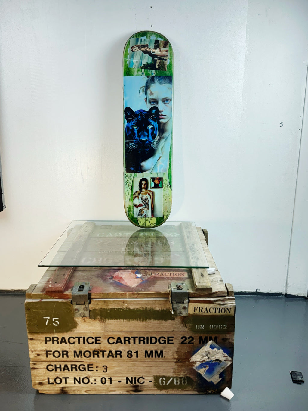 Skateboard 7 by David Bromley — portrait collage across green and pale blue skateboard surfaces, painted deck displayed above a glass-topped wooden crate.