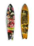 Skateboard 8 by David Bromley — bold poster lettering and yellow figurative imagery on a shaped skateboard deck, painted deck displayed above a glass-topped wooden crate.