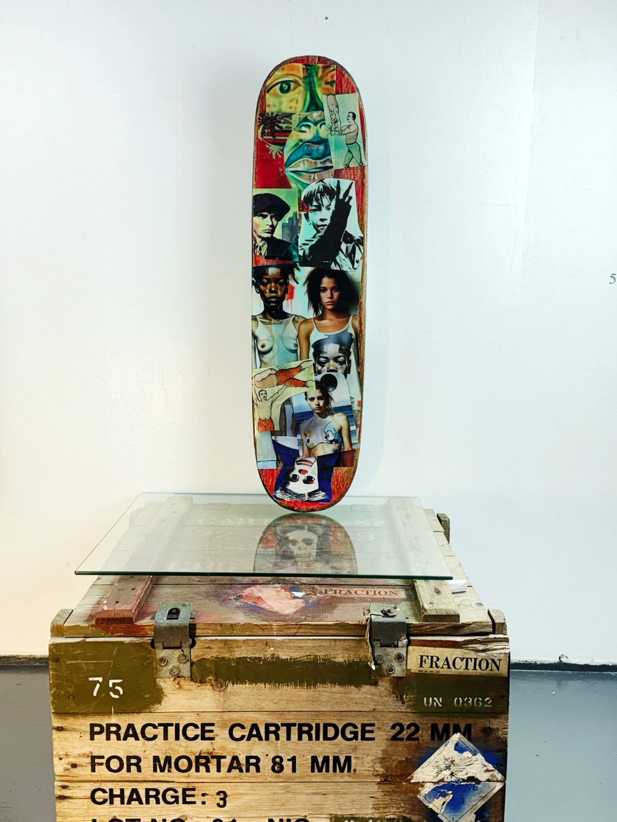 Skateboard 3 by David Bromley — blue-green collage and colourful portraits on a skateboard deck, painted deck displayed above a glass-topped wooden crate.