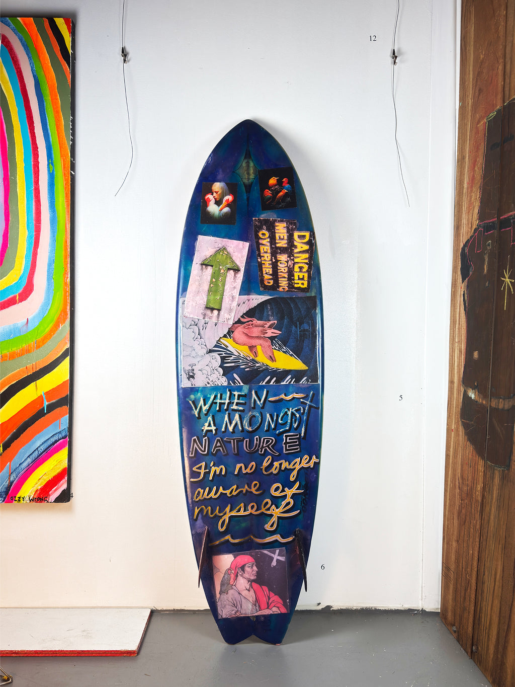 Danger Surfboard by David Bromley — blue lettered side standing in the gallery.