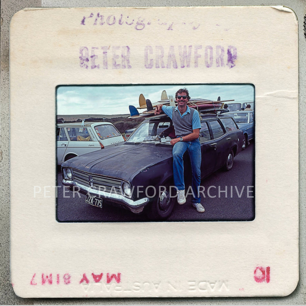 Vintage photograph slide of a man sitting on a car with surfboards, labeled 'Peter Crawford Archive'.