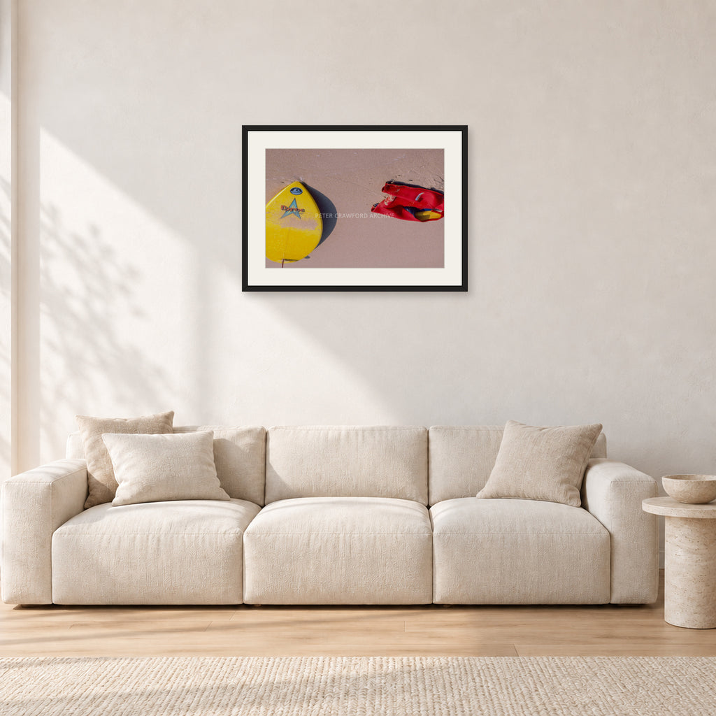 Bells Beach Overview, 1983 by Peter Crawford — 60 × 40 cm, black frame with white mat, shown in a light minimalist living room.