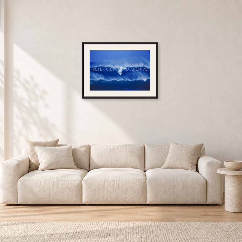 Big Sunset, Unknown Surfer by Peter Crawford — 60 × 40 cm, black frame with white mat, shown in a light minimalist living room.