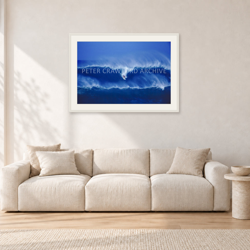 Big Sunset, Unknown Surfer by Peter Crawford — 90 × 60 cm, white frame with white mat, shown in a light minimalist living room.