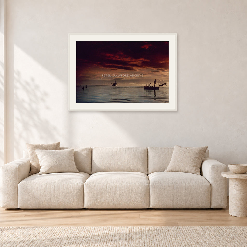 Fiji Sunset II by Peter Crawford — 90 × 60 cm, white frame with white mat, shown in a light minimalist living room.