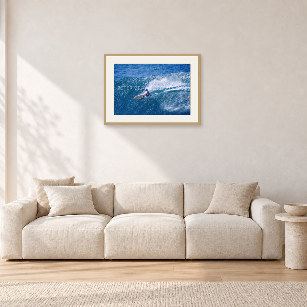 Honolua Bay, No Leash by Peter Crawford — 60 × 40 cm, hayseed frame with white mat, shown in a light minimalist living room.