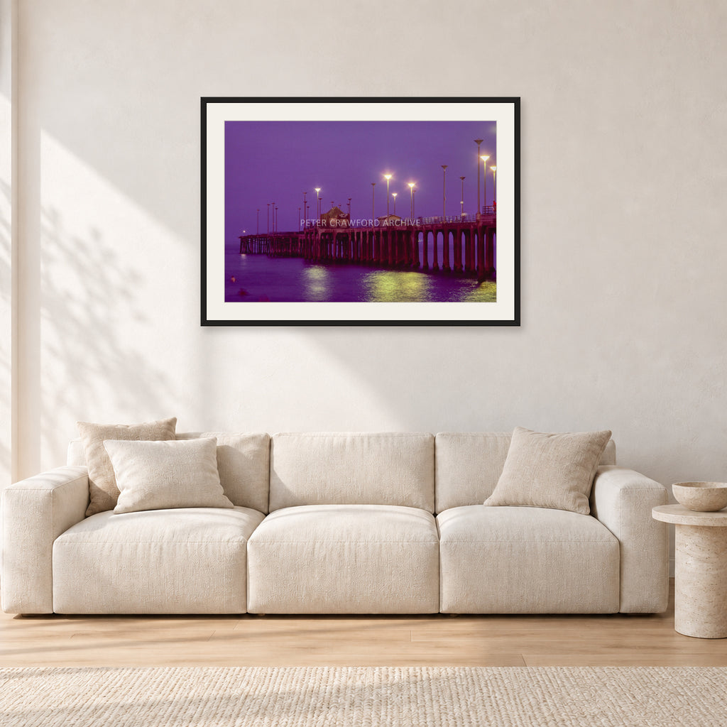 Huntington Pier by Peter Crawford — 90 × 60 cm, black frame with white mat, shown in a light minimalist living room.