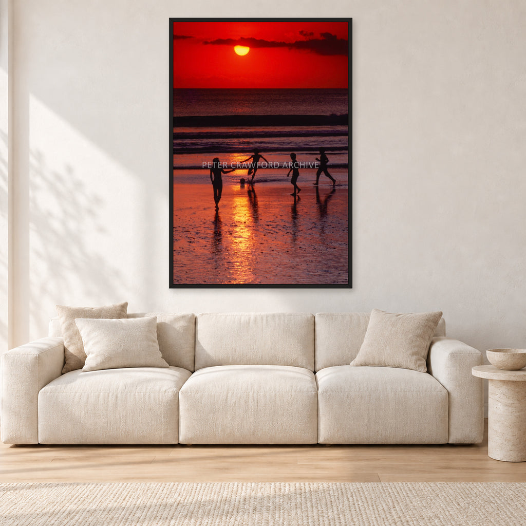 Indonesian Sunset Kids by Peter Crawford — 80 × 120 cm, black frame, shown in a light minimalist living room.