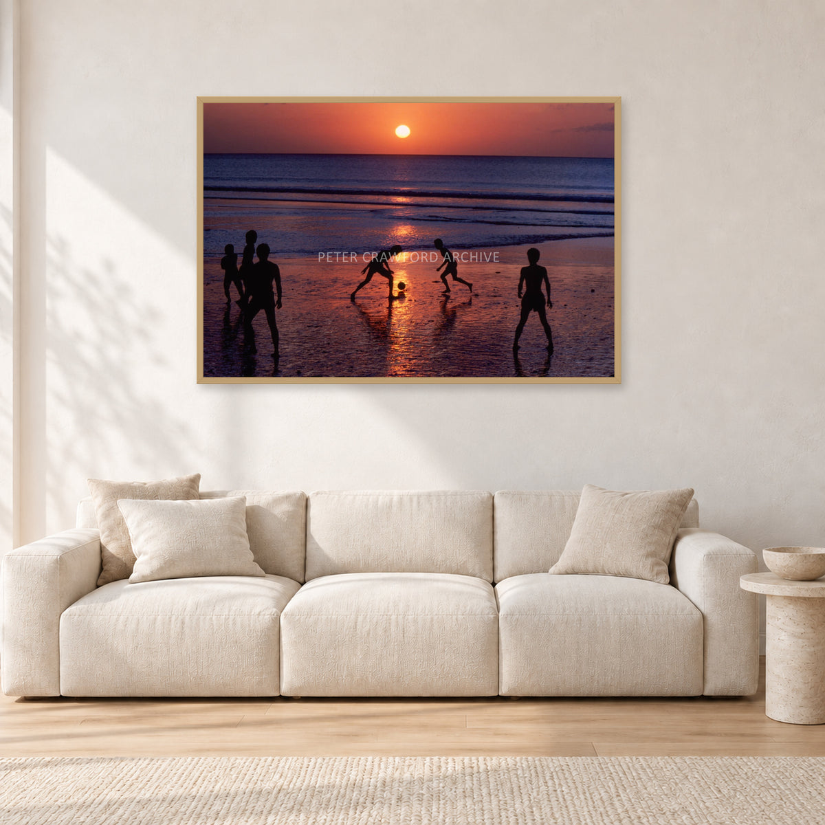 Kuta Kids Soccer, 1979 by Peter Crawford — 120 × 80 cm, hayseed frame, shown in a light minimalist living room.