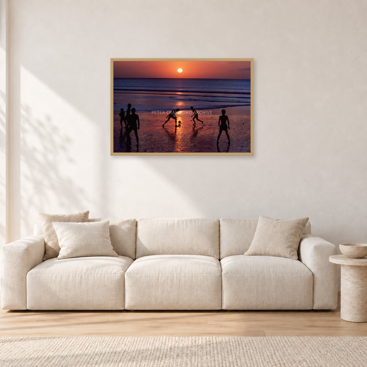 Kuta Kids Soccer, 1979 by Peter Crawford — 90 × 60 cm, hayseed frame, shown in a light minimalist living room.