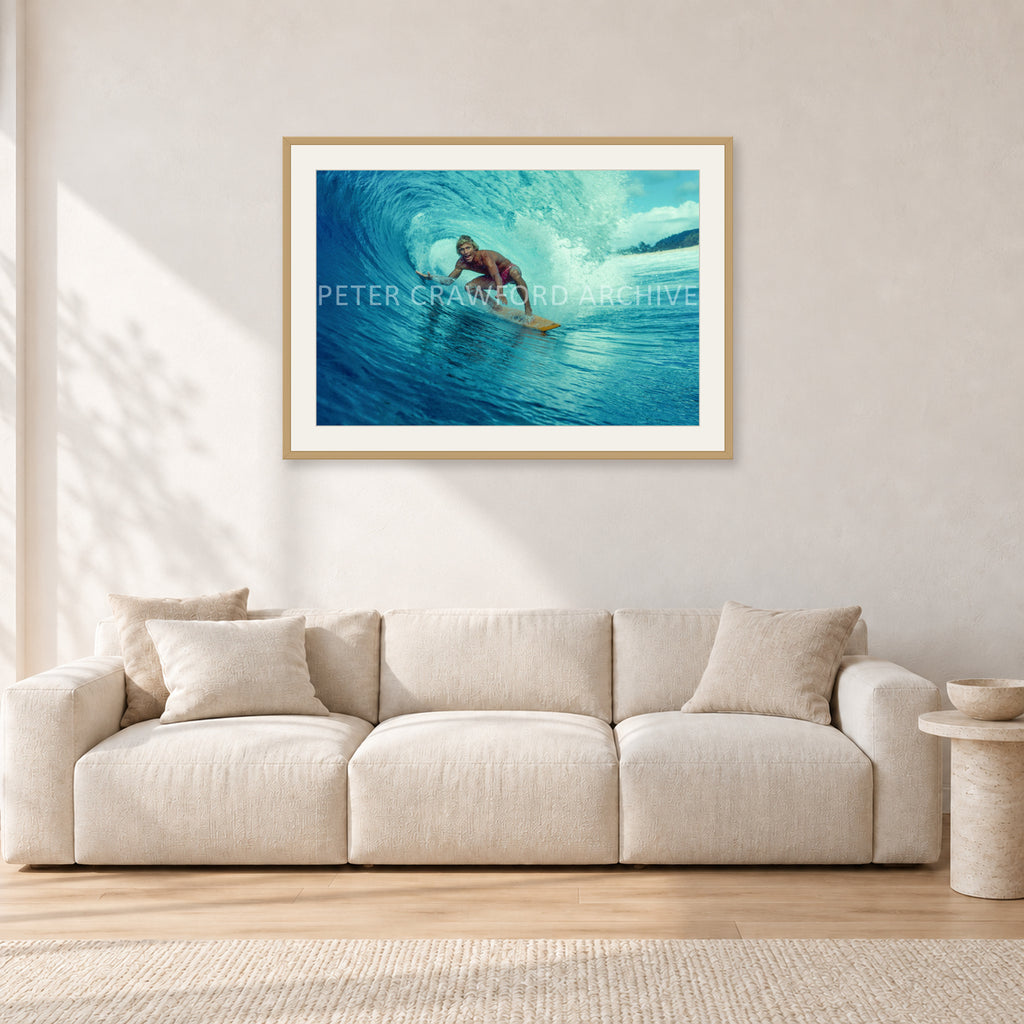 North Shore Tube Ride, Hawaii 1970s by Peter Crawford — 90 × 60 cm, hayseed frame with white mat, shown in a light minimalist living room.