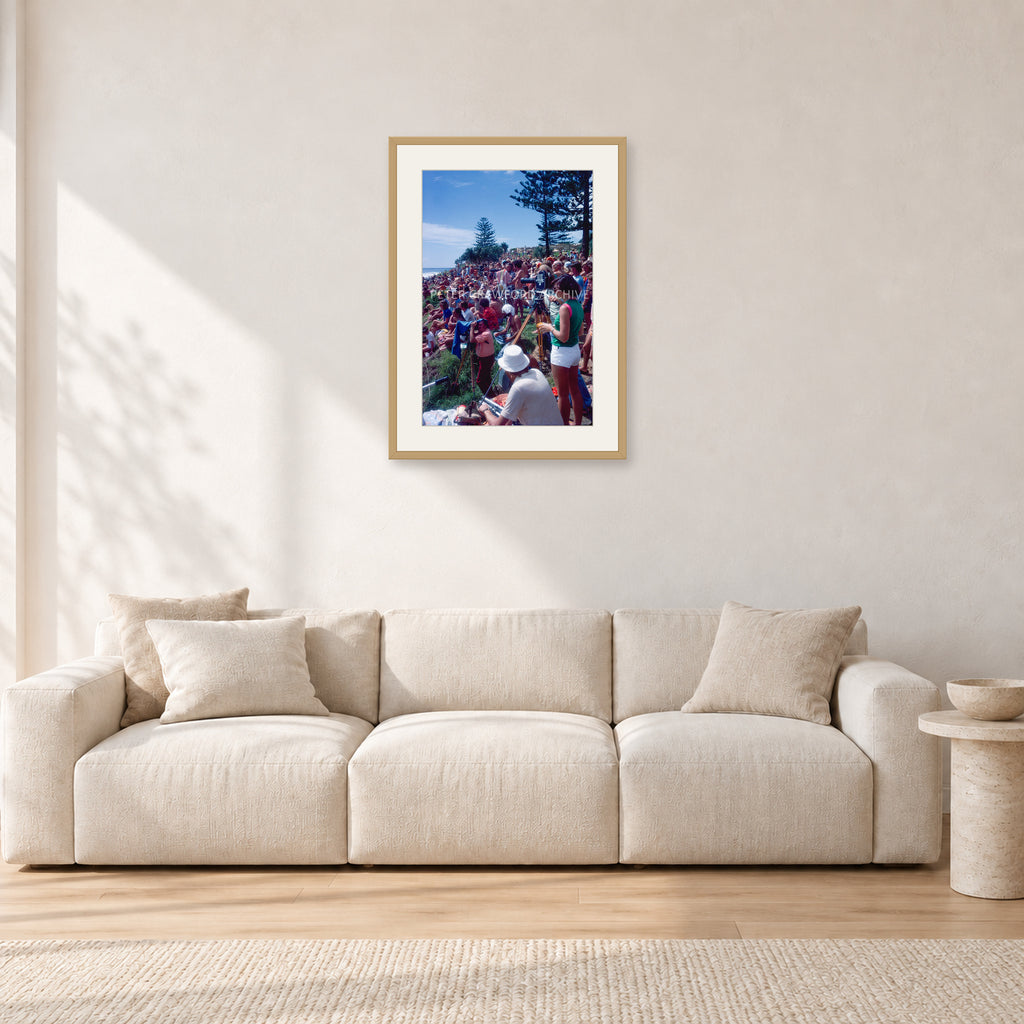 Stubbies Camera Crowd 78 Steve O'Ferral by Peter Crawford — 40 × 60 cm, hayseed frame with white mat, shown in a light minimalist living room.