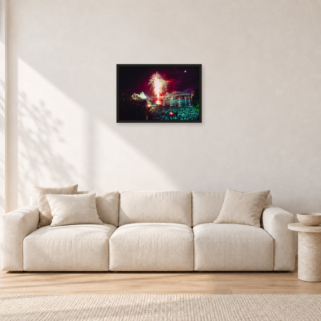 Tom Carroll and Aaron Chang, Waimea 1985 by Peter Crawford — 60 × 40 cm, black frame, shown in a light minimalist living room.