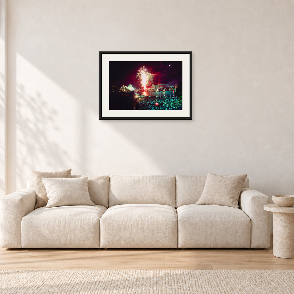 Tom Carroll and Aaron Chang, Waimea 1985 by Peter Crawford — 60 × 40 cm, black frame with white mat, shown in a light minimalist living room.