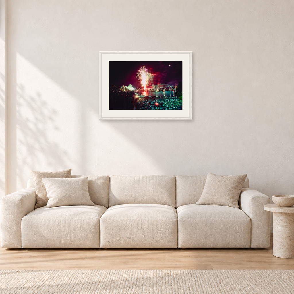 Tom Carroll and Aaron Chang, Waimea 1985 by Peter Crawford — 60 × 40 cm, white frame with white mat, shown in a light minimalist living room.