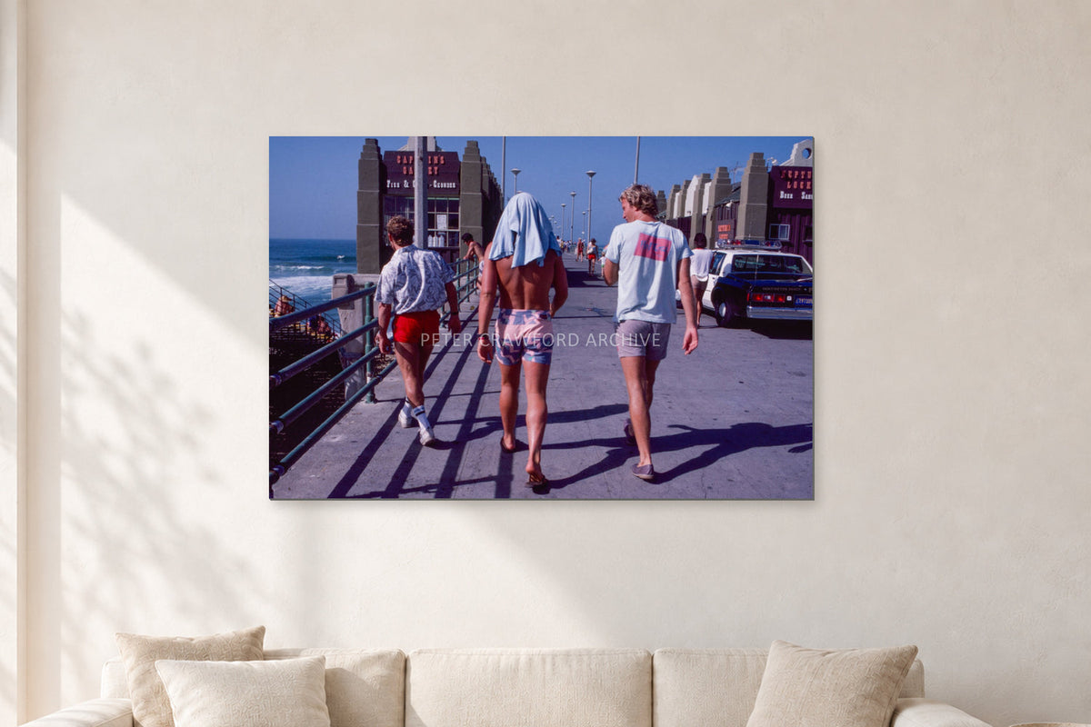 Tom Carroll, Mike Newling and Simon Anderson, Huntington 1984 by Peter Crawford — 120 × 80 cm, aluminium-mounted resin print, shown in a light minimalist living room.