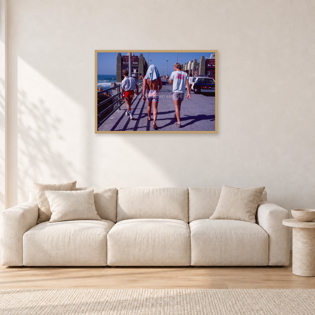 Tom Carroll, Mike Newling and Simon Anderson, Huntington 1984 by Peter Crawford — 90 × 60 cm, hayseed frame, shown in a light minimalist living room.