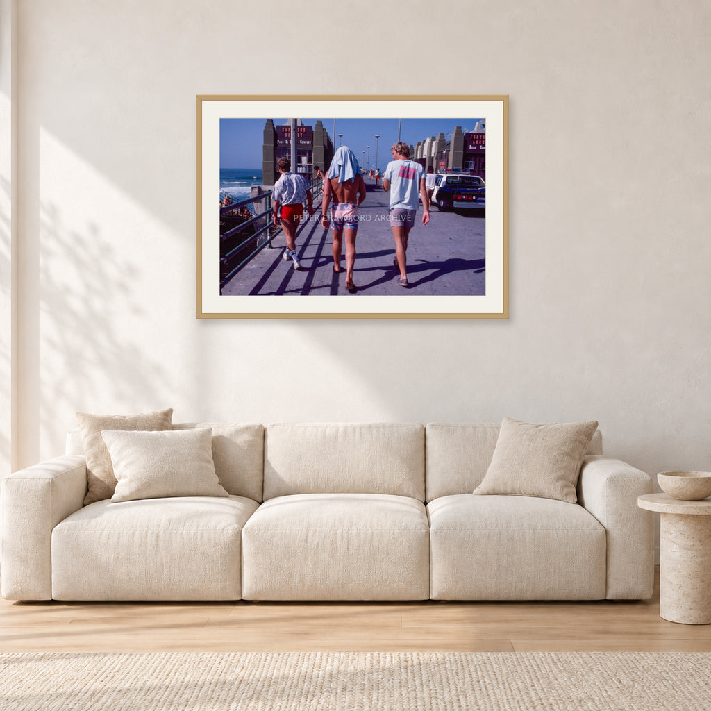 Tom Carroll, Mike Newling and Simon Anderson, Huntington 1984 by Peter Crawford — 90 × 60 cm, hayseed frame with white mat, shown in a light minimalist living room.